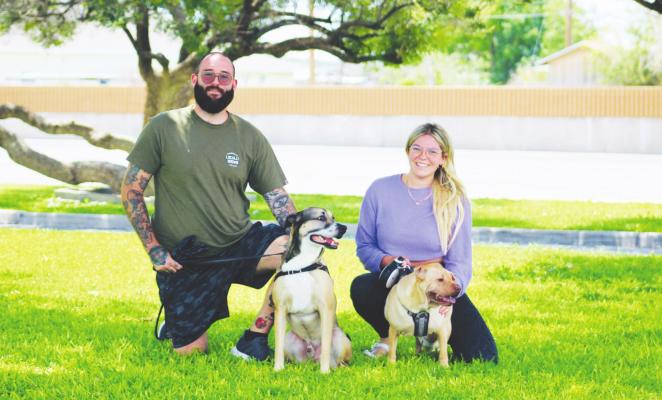 Mark and Kianna of California kneel in the grass with their dogs Moose and Squish during their first pass through Fort Stockton. Photo by Jeremy Gonzalez