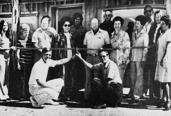 JUNE 1976 OPENING THE WINDMILL – Mayor Mike Walling (left) and Chamber President Jay Chancellor share the ribbon-cutting duties at the official Grand Opening of The Windmill, Fort Stockton’s new western wear outlet. In on the honors are owners, employees and friends: (L-R) Cynthia Williams, Betty Hickman, Peeberry White, Mrs. White, Raymond Gonzales, Jimmy Randle, Gerald Porter, Mrs. Randle, Mrs. Porter, Gene Day, SuZane Blackwelder, and Lila Urias. (Pioneer photo)