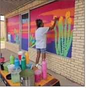 Vickie Bradshaw works on a colorful desert-themed mural Wednesday in downtown Fort Stockton as part of a beautification project transforming vacant storefront windows into public art. Bradshaw said each design is inspired by native West Texas landscapes and can take more than 13 hours to complete. Pioneer Photo by Tristian Barragan