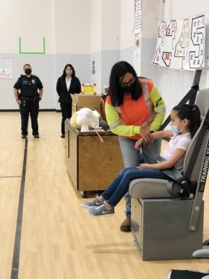TXDoT Traffic Safety Specialist Gina Galindo shows an Alamo Elementary volunteer how to properly buckle up with a booster seat. Sharing the floor with Galindo is SRO Rosalie Acosta and City of Fort Stockton Municipal Court Judge Maribel Perkins. Photo by Jeremy Gonzalez