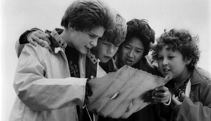 In a scene from the 80’s cult classic movie, “The Goonies,” young actors Corey Feldman, Sean Astin, Ke Huy Quan and Jeff Cohen look over a treasure map in hopes of finding enough gold and silver to save their neighborhood. Courtesy Photo